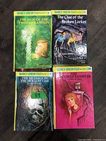 Photo shows four hardcover Nancy Drew books with titles visible: The Sign of the Twisted Candles, The Clue of the Broken Locket, The Message in the Hollow Oak, and The Crooked Banister.