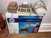 Setup showing all items together with the HP LaserJet Pro P1102w box, beige General Electric phone, Canon adding machine and Shredmaster shredder.