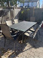 Rectangular patio table with six matching chairs arranged on stone patio under fence.