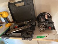 Rotozip spiral saw and Paslode nailer with case on shelf, yellow drill in background.
