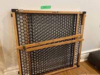 Safety 1st child safety gate folded and standing upright showing wood frame and black mesh center with circular cutouts.