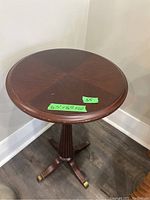 Round wooden side table with dark polished top, showing the full table with pedestal base and casters on feet.
