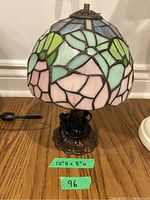 Full view of the stained glass lamp showing the colorful leaded glass shade and ornate bronze-colored base.