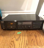 Full front view of AKAI GX-33 stereo cassette deck placed on wooden floor showing all front panel controls and cassette door.