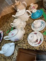 View of all assorted tea pots and fine china cups and saucers on granite counter