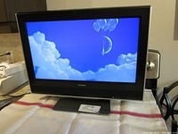 Front view of Toshiba 23-inch LCD TV powered on, displaying a blue background with clouds and balloons.