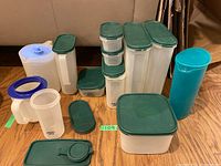Full lot of various Tupperware storage containers of different sizes with green lids, arranged on floor.