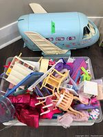 Wide view of the vintage Barbie airplane and large bin with assorted Barbie accessories including chairs, doll clothes, and furniture parts