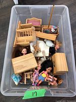 Plastic container holding wooden dollhouse furniture pieces, small dolls, and porcelain vases, top view.
