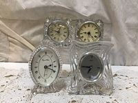 Five assorted crystal clocks with various shapes including square, oval, and abstract. Clear faceted crystal bodies with clock faces.