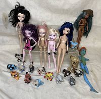 Overall lot with six Disney Descendants dolls and a collection of small animal figures posed on a white cloth background.