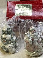 Photo of the Fitz and Floyd snow-themed salt and pepper shakers, one depicting Santa holding a white rabbit and the other a Christmas tree with white rabbits, wrapped in plastic with original packaging visible.