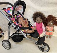 Three dolls shown with one seated in balloon-pattern stroller, two standing behind dressed in different outfits.