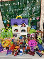 Front full view of toy assortment including learning toys, playhouse, vehicles, and plush toys arranged in front of a green alphabet playmat.