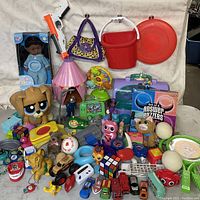 Wide view of the toy assortment showing a boxed doll, toy guns, plush animals, toy cars, and puzzles.