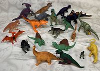 Photo showing 20 assorted toy dinosaurs of various species and colors placed on a white cloth background.