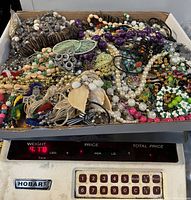 Top-down photo of mixed vintage to modern broken jewelry pieces, beads, pearls, fabric elements and metal charms in a box.
