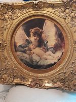 Front view of circular antique print showing angel and baby in ornate gilded frame
