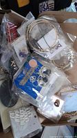 Box with assorted costume earrings in packets and packaging, showing mixed styles including hoops and studs.