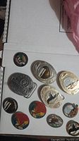 Photo of 4 belt buckles and 7 pins laid out on white cardboard showing various Alaska imagery