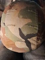 Close-up front and top view of the camouflage helmet showing the woodland camo fabric covering and sewn ventilation slits.