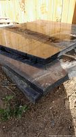 Three stacked black granite slabs on a dirt floor, showing their thickness and rough edges