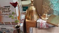 Photo showing tall brass bell, metal rose flower in brass vase, and smaller brass bell