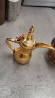Full view of brass tea pot showing handle, spout and lid in closed position, with reflective brass surface and some scratches.