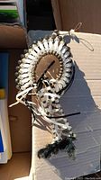 Native American chief head dress with white shell-like beads laid in fan shape, black feathers and leather ties visible in a cardboard box