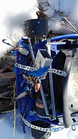 Blue go kart frame showing seat, steering wheel, exposed wiring and electrical module, placed on snow-covered ground.