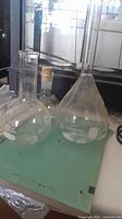Several clear glass laboratory flasks including a 1000 ml volumetric flask and round bottom flasks on a green surface.