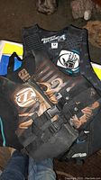 Photo shows black and brown Jetpilot child life vest with multiple straps and buckles in front of a black Body Glove vest, indicating two life vests in the lot.