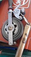 Close-up photo of the hand cable pulley tool showing the coiled cable, metal frame, and wooden handle.