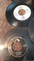 Photo showing close-up of two 45 RPM vinyl records, one RCA Victor labeled 'Tango Americano' by Buddy Merrill and one labeled 'Star' with partial text visible.