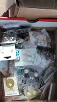Box containing assorted earrings in original packaging, various styles and colors visible including studs, drops, and decorative shapes
