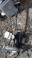 Full view of trolling motor laid on rocky ground showing propeller, shaft and control box.