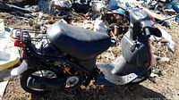 Side view of black Honda moped scooter showing body, seat, floorboard and missing mirror.