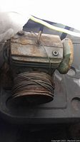 Side angle showing rusted, metal heavy duty winch with thick cable wound on drum and hook attached to cable.