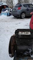 Close-up side view of metal compressor pump placed outdoors on snow with a visible large pulley wheel and cooling fins.