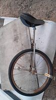 Side view of the vintage unicycle showing the tire, seat post, and black seat with some rust on the metal parts