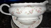 Close-up of white gravy boat with pink rose floral pattern and gold plated trim, showing some wear and fading