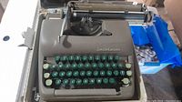 Vintage Smith-Corona typewriter housed in a case showing the entire device and keyboard area with green round keys.