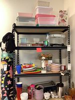Four tier metal shelving unit filled with kitchen storage bins, colorful plastic bowls, glass bakeware, kitchen tools, cups, and flatware.
