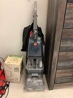 Full upright view of Hoover SpinScrub 50 carpet cleaner in grey and blue with attached power cord and accessories like black carrying bag.