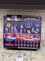 Front image of 2020 Battle for the White House chess set packaging showing the themed chess pieces on a chessboard with red and blue square bases.