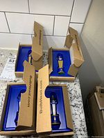 Four commemorative chess pieces each in individual blue plastic trays inside cardboard boxes marked BulbHead.com, arranged on granite counter