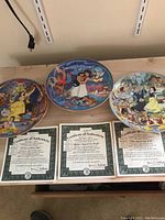 Three Walt Disney commemorative plates featuring Beauty and the Beast, Aladdin, and Snow White along with their certificates of authenticity.