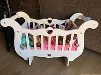 White wooden doll crib with heart shaped cutouts holding blanket, pillow and nine Ty Beanie Babies.