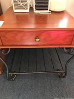 Front view of wooden topped table showing drawer with brass knob and metal curved legs base.