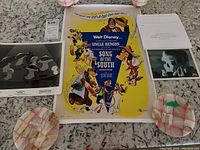 Photo of Song of the South lobby card with colorful character illustration and text, placed on a marble countertop with decorative plates.
